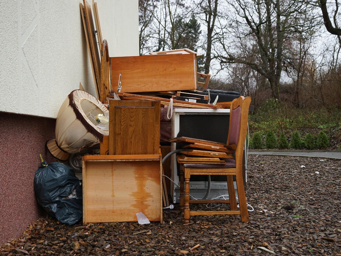 Old cabinets, a chair, a lamp and an appliance stacked outside for removal